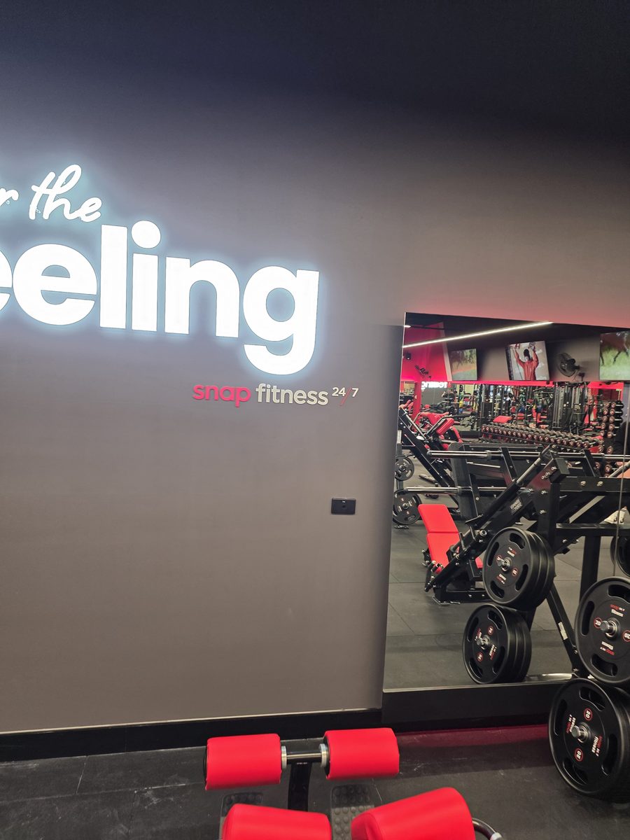 Illuminated Snap Fitness 24/7 signage above the mirrored weights area