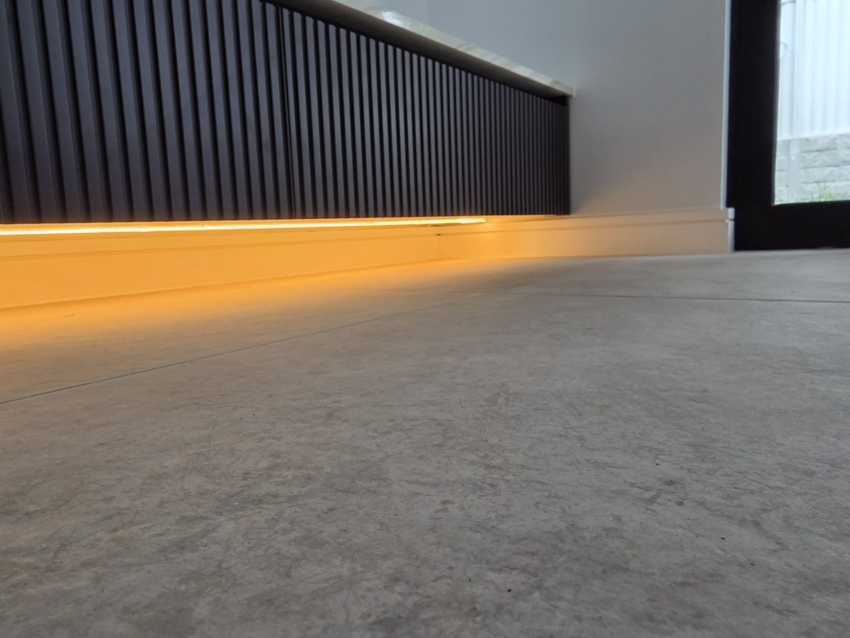 After, LED on: warm toe-kick LED floor-wash under the same fluted joinery, Picnic Point duplex